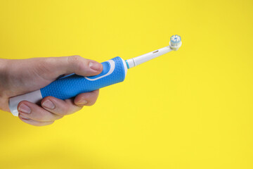 Modern electric toothbrush in hand on yellow background, oral hygiene concept