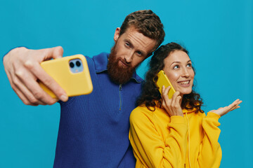 Woman and man funny couple with phones in hand taking selfies crooked smile fun, on blue background. The concept of real family relationships, talking on the phone, work online.