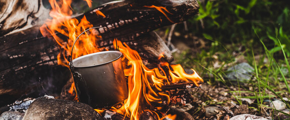 Kettle hanging over fire. Cooking food at fire in wild. Beautiful big log burns in bonfire...