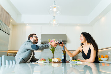 Excited couple saying cheers while drinking wine in a luxury kitchen