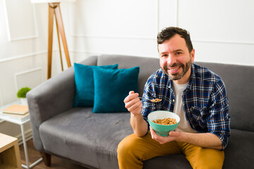 Smiling cheerful man eating breakfast relaxing on the sofa