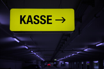 Yellow glowing KASSE information sign in an underground car park with white neon lighting