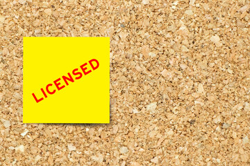 Yellow note paper with word licensed on cork board background with copy space