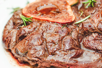 Cooked braised beef steak on the bone ossobuco with pepper, rosemary on the board.