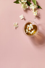 Cup of jasmine tea with jasmine flowers on a pink pastel background. Organic natural drinks concept. View from above. Copy space.