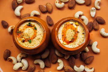 Obraz na płótnie Canvas Kulfi ice cream in two clay pots on a solid orange background with cashews and almonds. Kulfi is a popular traditional Indian dessert made of milk with spices and nuts