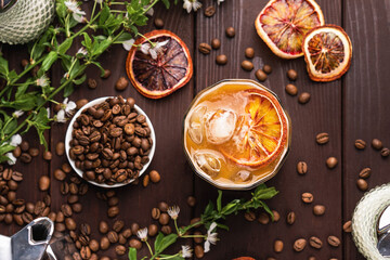 Iced coffee with milk and orange slices on dark wooden table with coffee beans. Summer drink