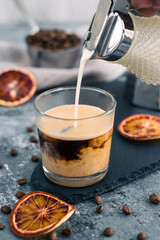 Iced coffee with milk. Summer drink. Pouring milk in coffee with ice cube on grey background