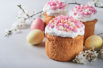 Traditional Easter sweet bread or cakes with white icing and sugar decor, colored eggs and cherry blossom tree branch over white table. Various Spring Easter cakes. Happy Easter day. Selective focus.