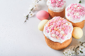 Traditional Easter sweet bread or cakes with white icing and sugar decor, colored eggs and cherry blossom tree branch over white table. Various Spring Easter cakes. Happy Easter day. Selective focus.