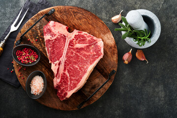 Thick Raw T-Bone Steak. Dry-aged Raw T-bone or porterhouse beef meat Steak on cutting boar with herbs and salt on dark background. Top view and copy space.