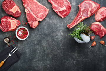 Raw prime steaks. Variety of fresh black angus prime meat steaks T-bone, New York, Ribeye, Striploin, Tomahawk on black or gray stone background. Set of various classic steaks. Top view, copy space.