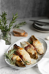 Braised chicory with ham, endives on a light stone background. Traditional Belgian cuisine.