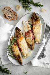 Braised chicory with ham, endives on a light stone background. Traditional Belgian cuisine.