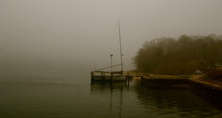 Silhouette of a sailboat and dock on a foggy morning