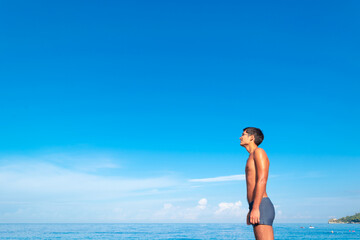 The figure of a young tanned guy on the beach against the background of the blue sea and sky.