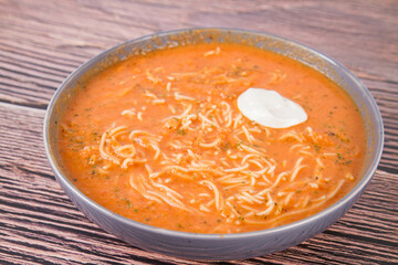 Tomato soup with noodles and a spoonful of cream on a wooden background