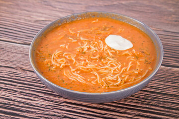 Tomato soup with noodles and a spoonful of cream on a wooden background