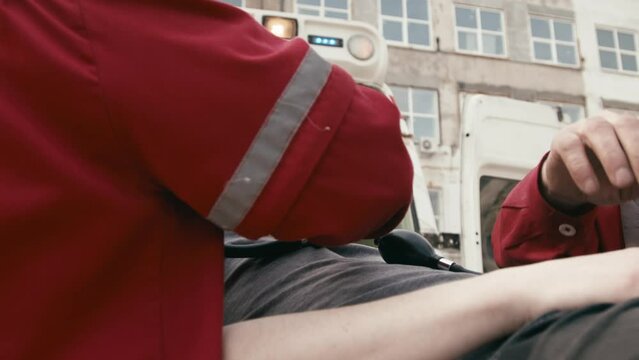 A team of ambulance paramedics provide emergency care and help an injured young man. Ambulance assistants arrived at the scene of a traffic accident on the street.
