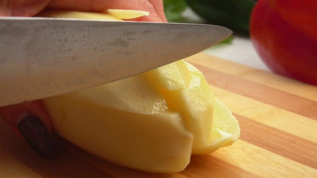 Knife cuts potatoes into squares on a wooden board