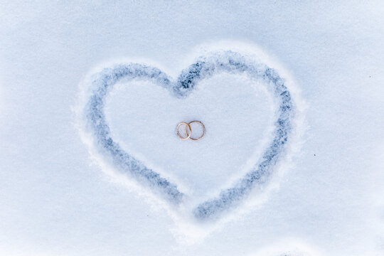 zwei Ringe in einem Herz aus Schnee bei einer Winterhochzeit