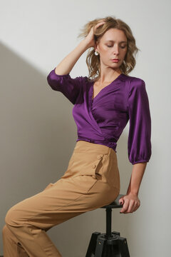 Serie of studio photos of young female model wearing violet silk satin wrap blouse and beige high rise trousers