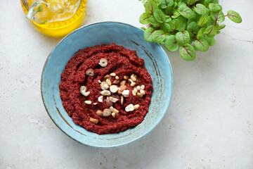 Turquoise bowl with beetroot paste and nuts, high angle view on a light-beige stone background, horizontal shot