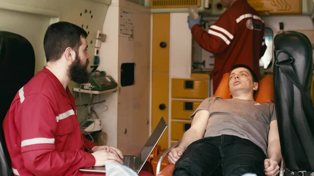 life saving concept. A professional paramedic uses a laptop to complete an injured patient's questionnaire on the way to the hospital. A paramedic works in an ambulance