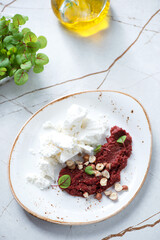White oval plate with feta cheese, beetroot caviar and nuts, vertical shot on a white marble background, selective focus