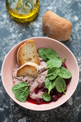 Liver pate served with cranberry sauce and fresh spinach in a roseate bowl, vertical shot on a dark-brown granite background