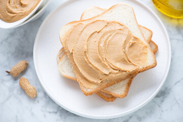 Sandwiches with peanut butter on a white plate, horizontal shot on a light-grey marble background, elevated view