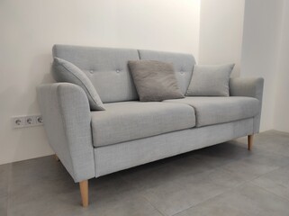 Light, gray sofa on wooden legs with pillows in a bright room