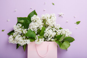 Pink bag full of lilac flowers. Bouquet of lilac on purple background. Surprise for lovely woman. Natural spring symbol. Aromatherapy.  Flowers Shopping. Flat lay, top view. Background with copy space
