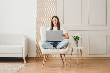 Full length portrait of a happy woman holding laptop computer while sitting on a chair