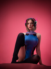 sexy gamer girl in a revealing bright bodysuit and gaming headset on a pink background