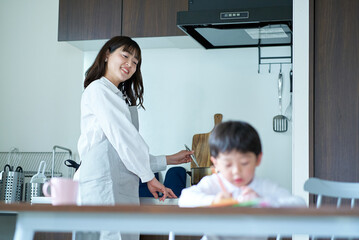 お絵描きをする子供と、家事をしながら見守る母親 © maru54