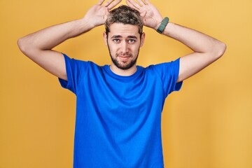 Hispanic man with beard standing over yellow background doing bunny ears gesture with hands palms...