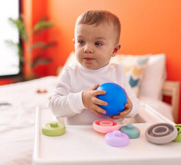 Adorable blond toddler sitting on highchair playing at bedroom
