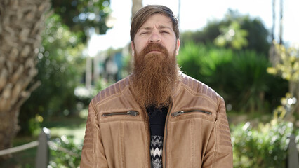 Young redhead man standing with serious expression at park