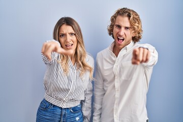 Young couple standing over blue background pointing displeased and frustrated to the camera, angry and furious with you