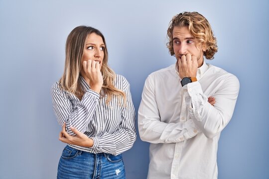Young couple standing over blue background looking stressed and nervous with hands on mouth biting nails. anxiety problem.