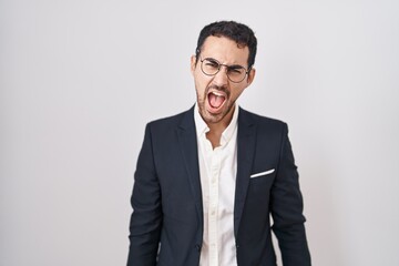 Handsome business hispanic man standing over white background angry and mad screaming frustrated and furious, shouting with anger. rage and aggressive concept.