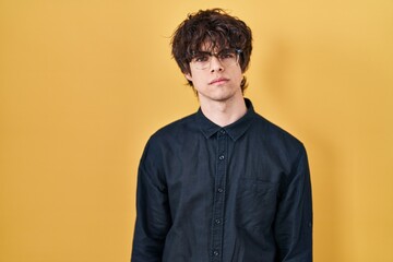 Young man wearing glasses over yellow background skeptic and nervous, frowning upset because of problem. negative person.