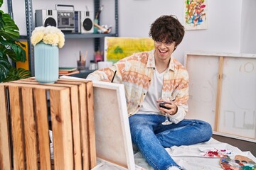 Young hispanic man artist drinking wine drawing at art studio