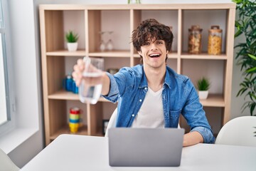 Young hispanic man using laptop drinking water at home