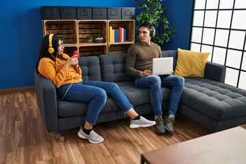 Man and woman couple using laptop and listening to music at home