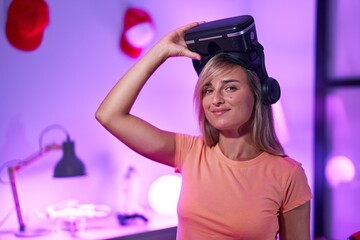 Fototapeta na wymiar Young blonde woman streamer smiling confident wearing virtual reality glasses at gaming room