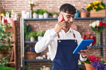 Young hispanic man florist talking on smartphone using touchpad at florist