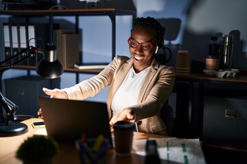 Beautiful black woman working at the office at night looking at the camera smiling with open arms for hug. cheerful expression embracing happiness.