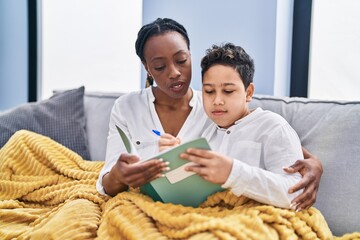 African american mother and son doing homework sitting on sofa at home